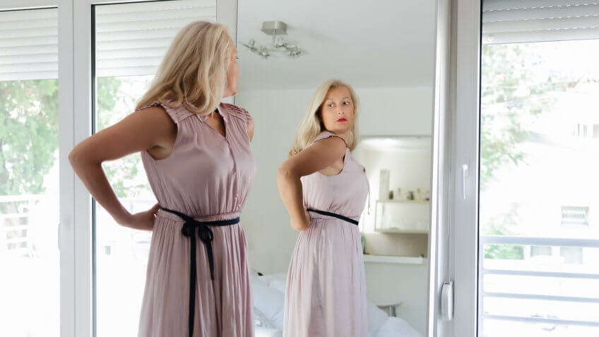 Senior woman standing in front of mirror wearing a long pink dress.