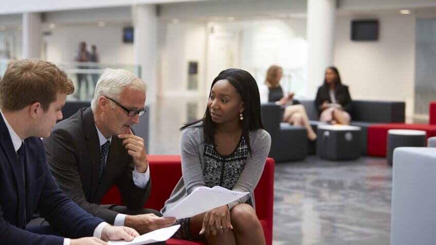 Businesspeople Discuss Document In Lobby Of Modern Office.