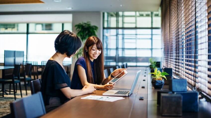 Business as usual in a modern Japanese or Korean office where two businesswomen working together on financial statements, budget clarification and project management.