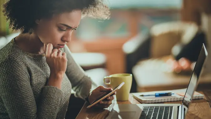 Young black woman reading a problematic text message on her mobile phone while working at home.