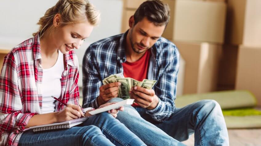 young couple counting money while sitting on floor in new apartment.