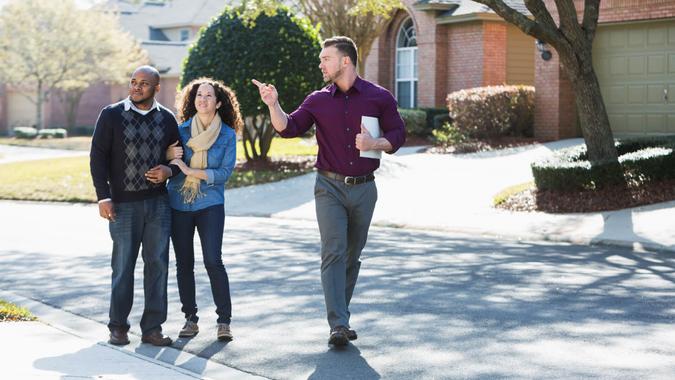 An African American couple walking on a residential street, with a young man holding a folder.