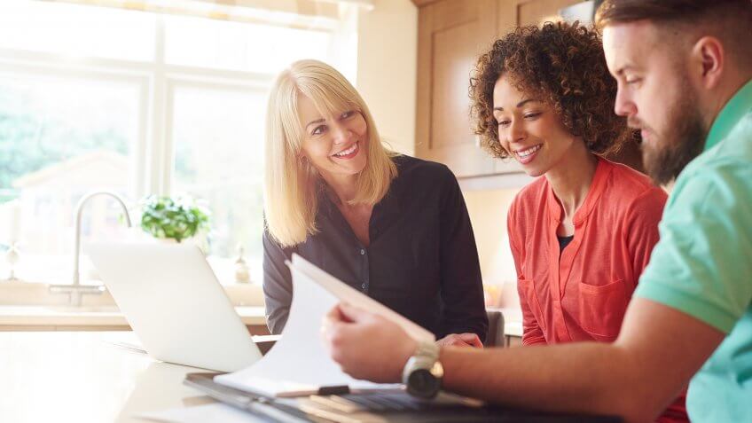 a couple sit in the kitchen of a show home and discuss some figures with the estate agent or mortgage advisor.