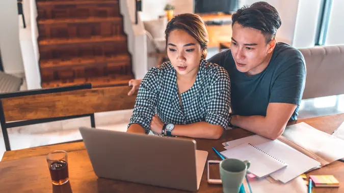 Serious young couple planning budget over laptop at table.
