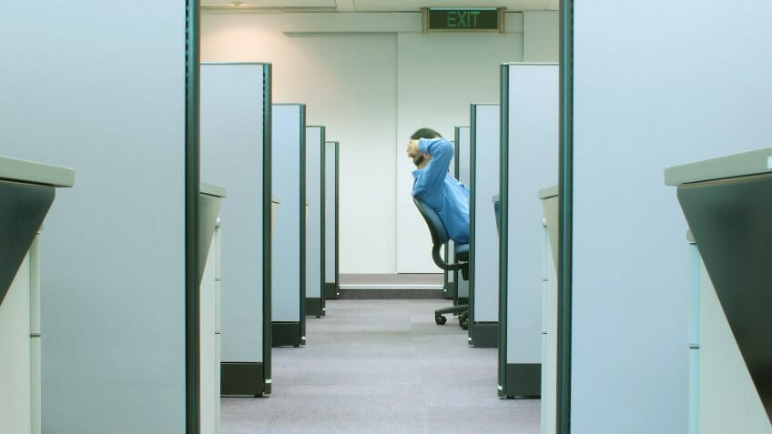 man reclining on his chair in cubicle with EXIT sign above.