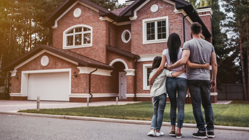 Back view of happy family is standing near their modern house and hugging.