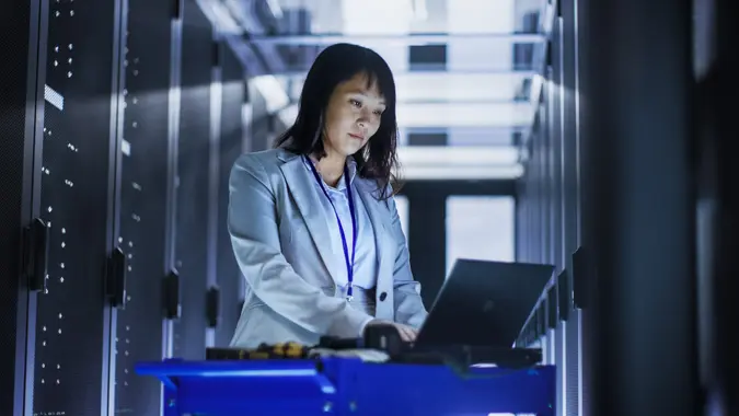 Asian Female IT Engineer Working on a Laptop on Tool Cart, She Scans Hard Drives.