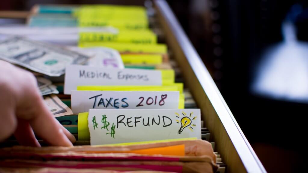 Tax refund conceptual tax season tax preparation photography with files and tax forms in filing cabinet and words refund and taxes 2018 written on file folders with light bulb for ideas and US dollar cash in background.