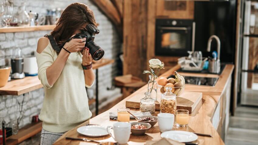Young female photographer taking photos of breakfast table in the kitchen.