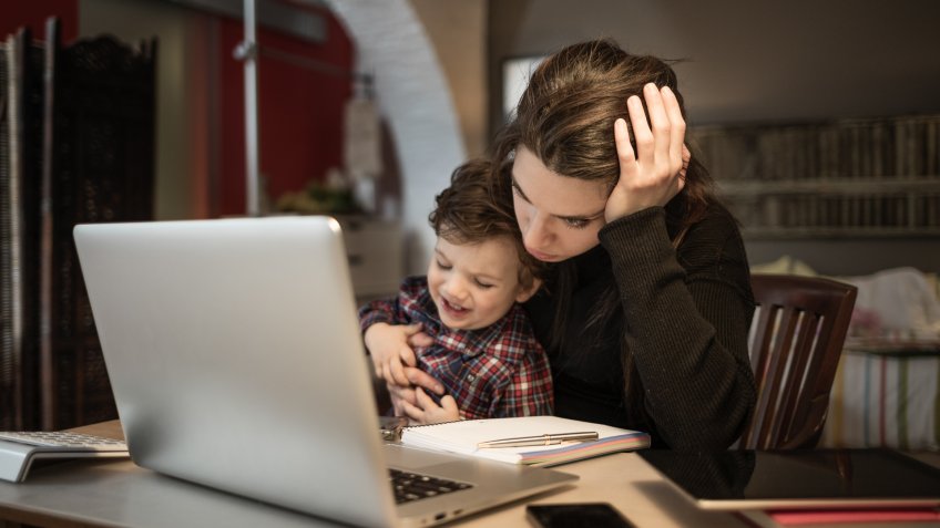 Worried woman working at home and holding her crying little son.