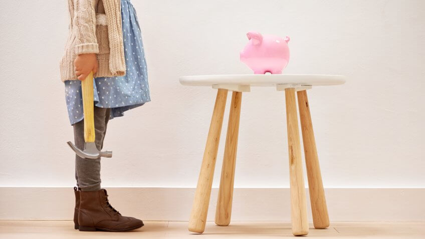 A kid with a hammer approaching a piggy bank