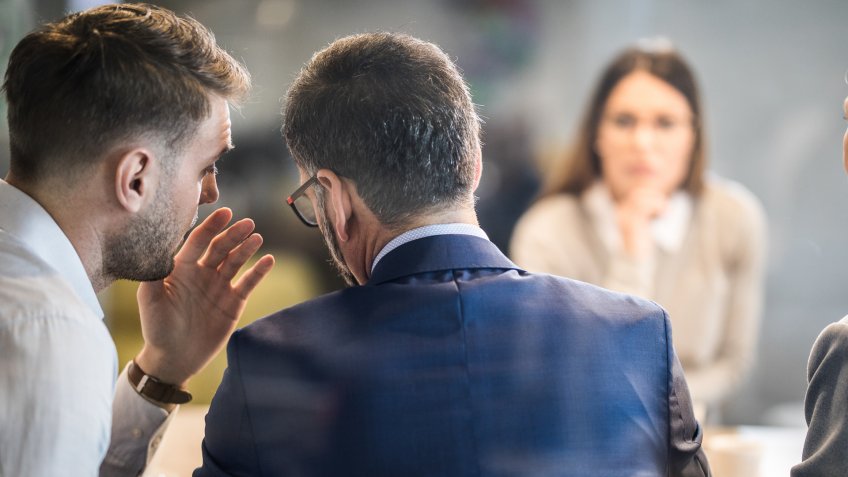 Male member of human resource team whispering to his colleague during a job interview in the office.