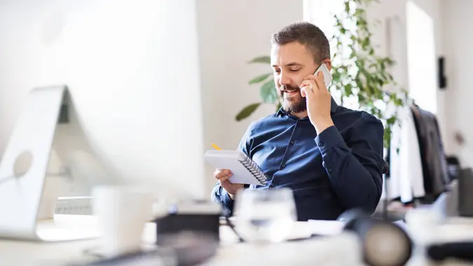 Businessman in wheelchair with smartphone at the desk in the office, making a phone call.