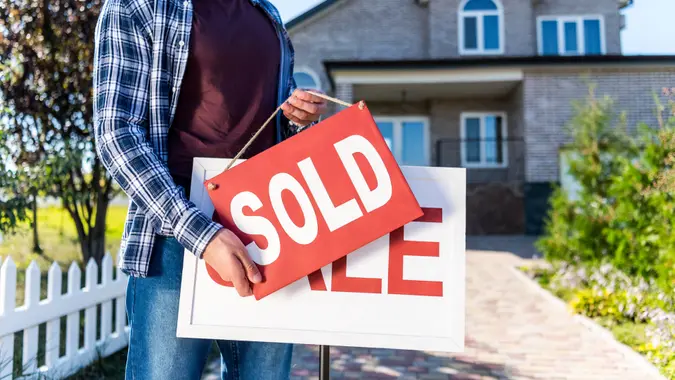 man hanging sold sign in front of house.