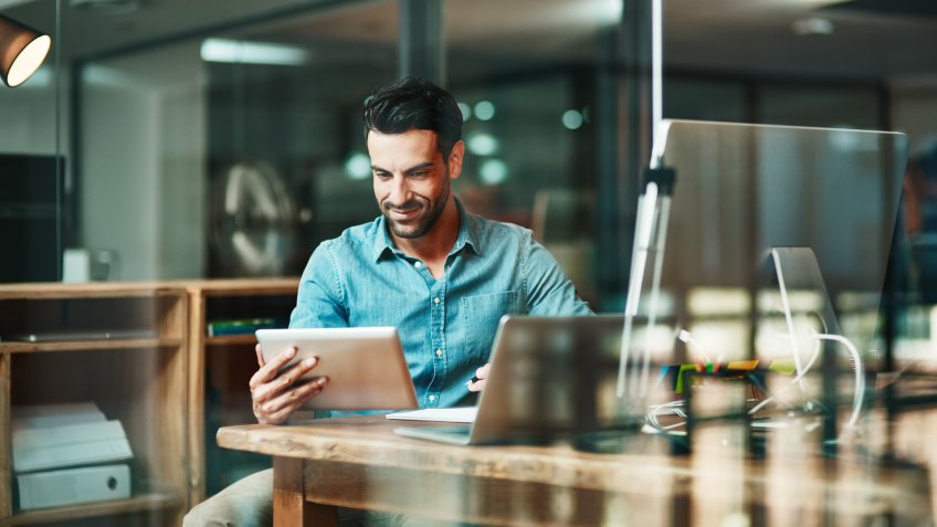 Shot of a young businessman using a digital tablet at his desk in a modern office.