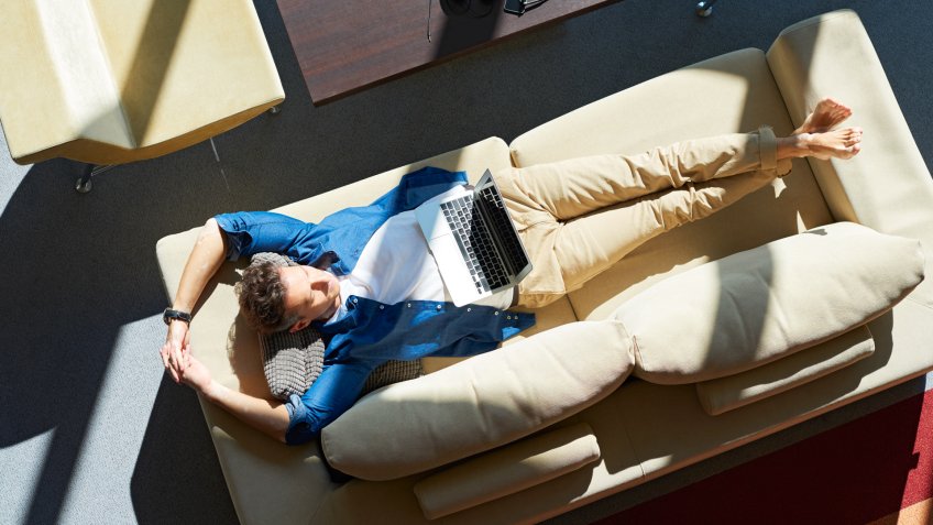 Full length shot from above of a closed eyes middle aged man lying on sofa and relaxing at home.