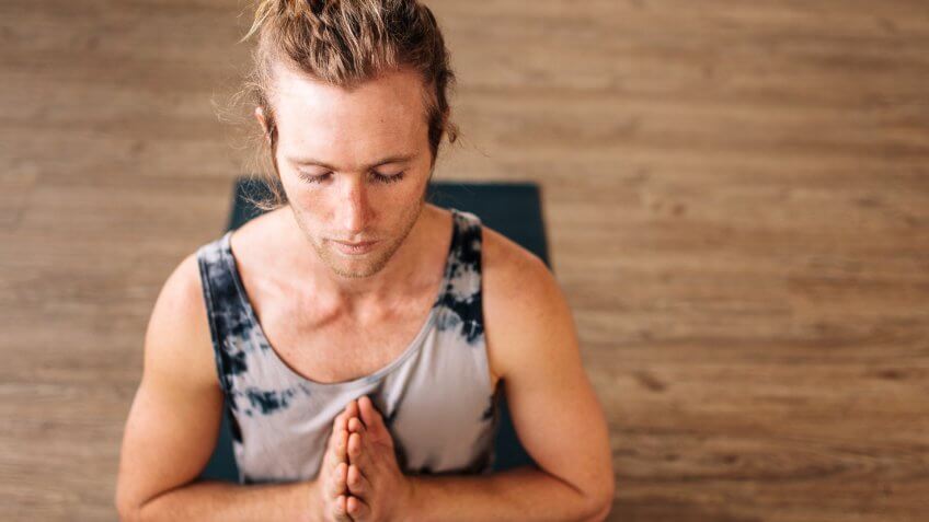 Over head view of fit young man practice yoga sitting on floor with his hands joined.