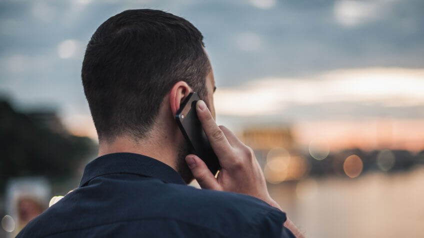 Businessman talking on mobile phone at sunset looking at evening city.