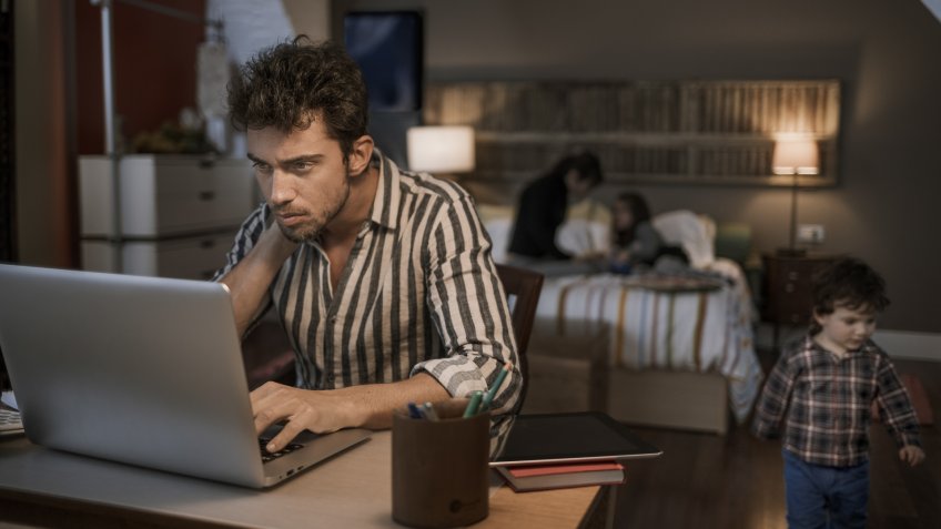 Man working late with laptop with family in the background.