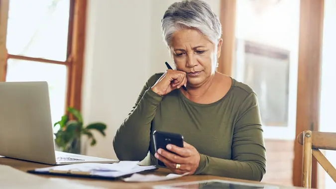 mature woman using a cellphone while going through paperwork at home.