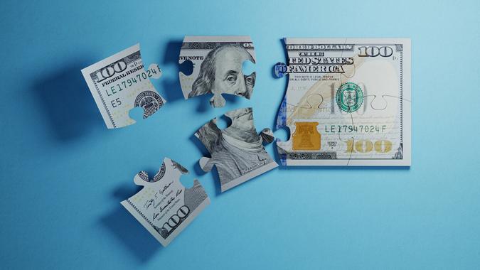 Jigsaw puzzle pieces textured with one hundred American dollar banknote on blue background.