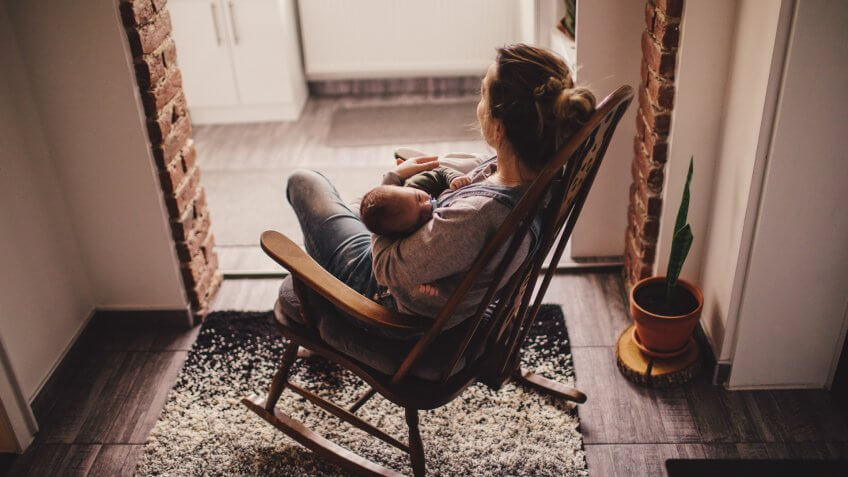 young mother holding her newborn baby, while sitting in a rocking chair.