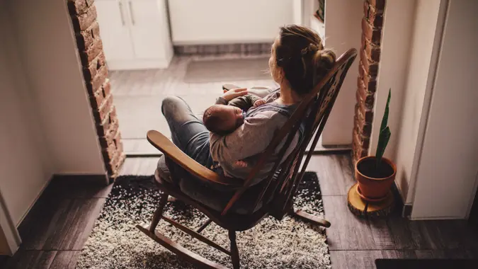 young mother holding her newborn baby, while sitting in a rocking chair.