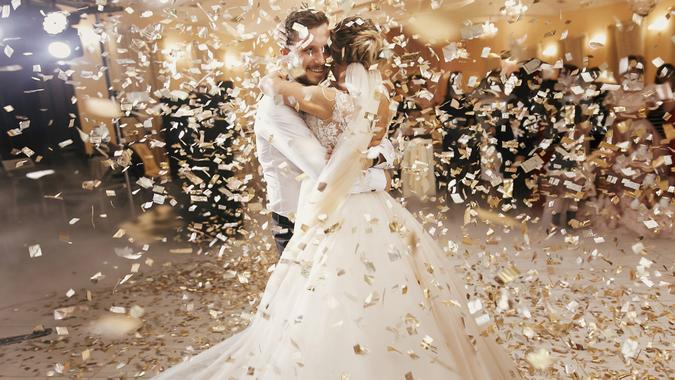 Gorgeous bride and stylish groom dancing under golden confetti at wedding reception.