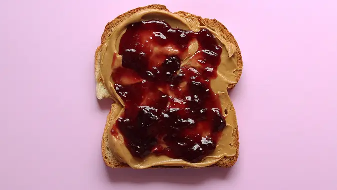 Open face peanut butter and jelly sandwich against purple background.