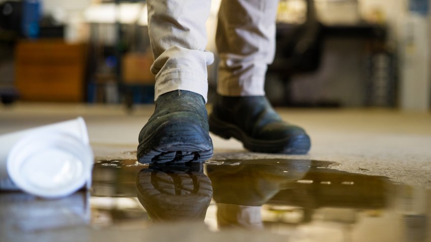 A male worker wearing work boots in a warehouse walking into a liquid spill on the floor.