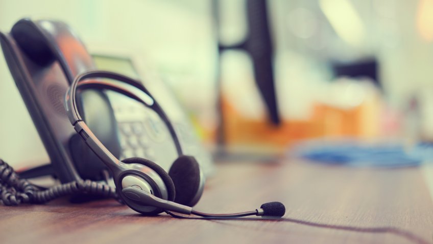 close up focus on call center headset device headset VOIP system with telephone answer machine technology at operation office desk for hotline telemarketing and network operator concept.