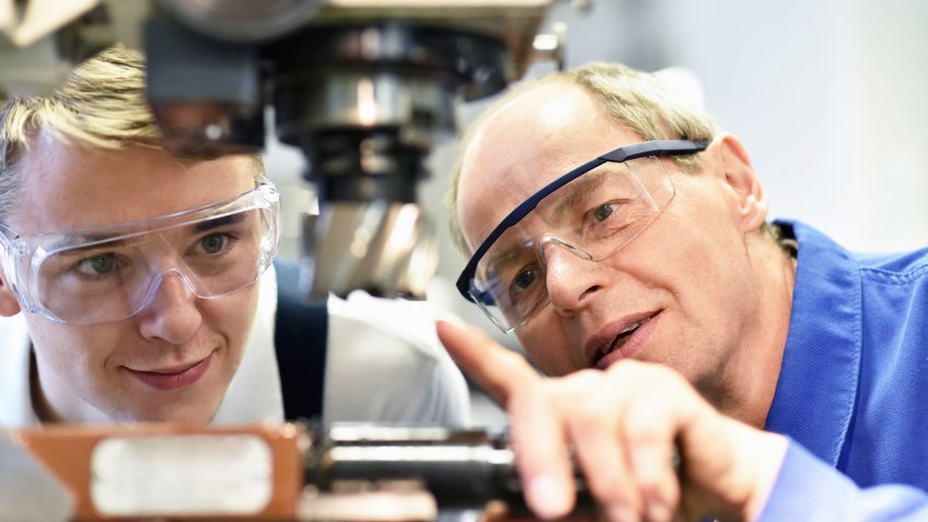 closeup picture: trainer and apprentice in vocational training on a milling machine - teacher explains details of the machine.