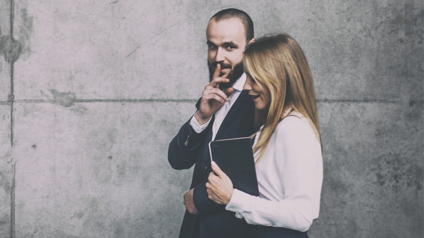 Businessman and businesswoman walking and sharing office rumors.