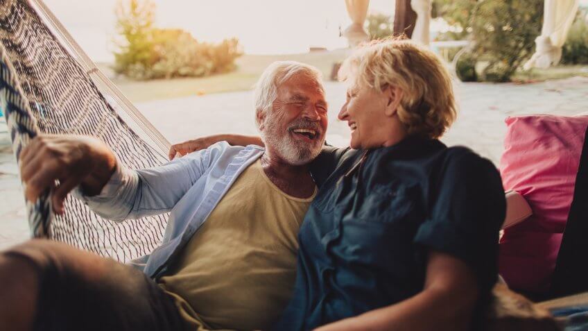 Photo of a senior couple having a relaxing moment in a hammock on a terrace of their family home by the sea.