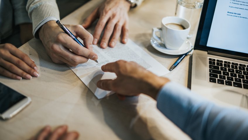 Unrecognizable man signing a contract while financial advisor is aiming at the place he need to sign.