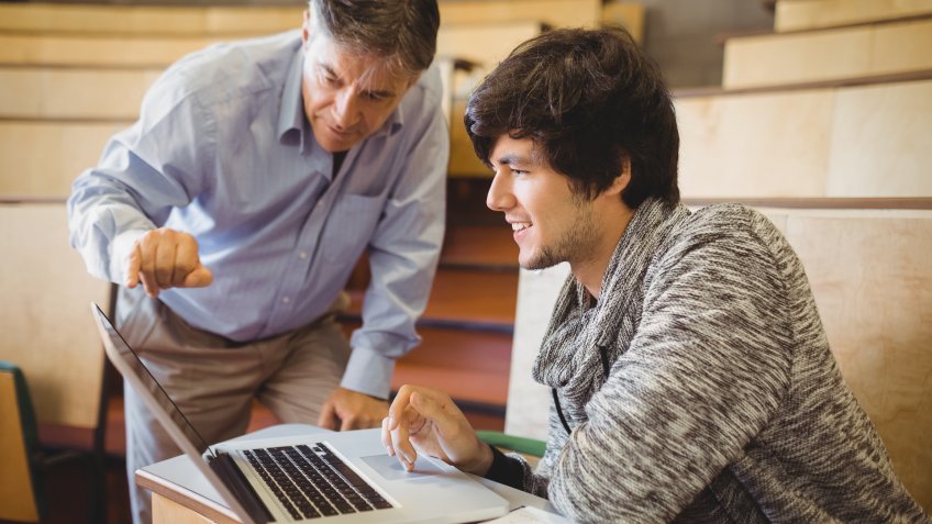 Professor helping a student in classroom at college.
