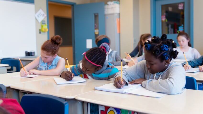 Multi-ethnic schoolgirls and shcoolboys sit into the class for their first day at school.