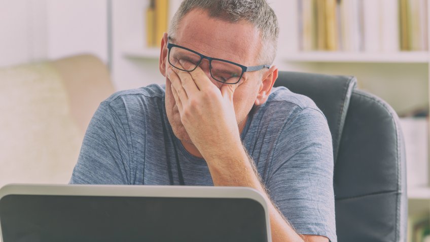 Tired freelancer man rubbing his eyes while working with laptop.