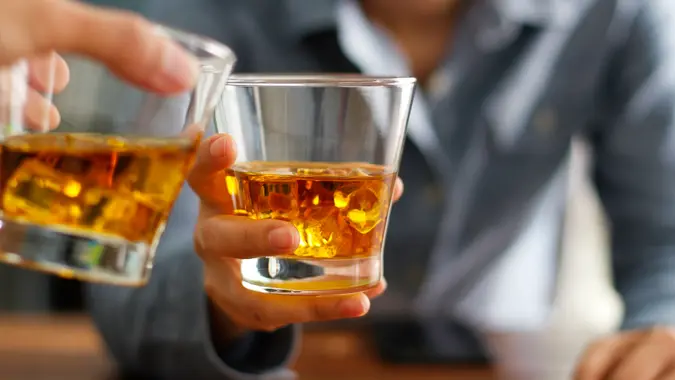 Close-up two men clinking glasses of whiskey drink alcohol beverage together at counter in the pub.