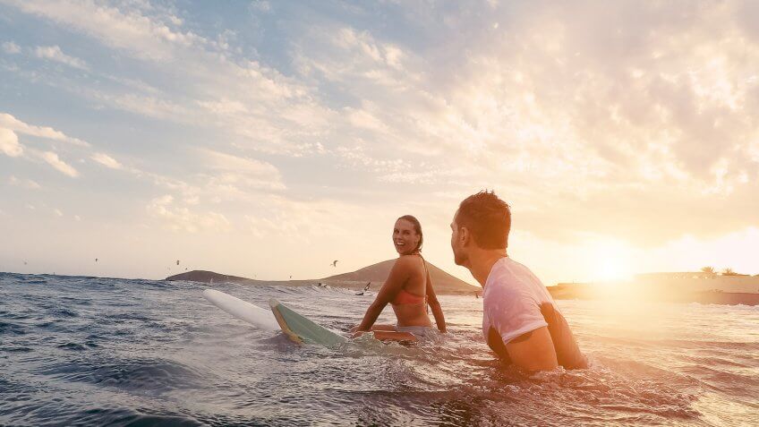 two surfers in the ocean with surfboards at sunset