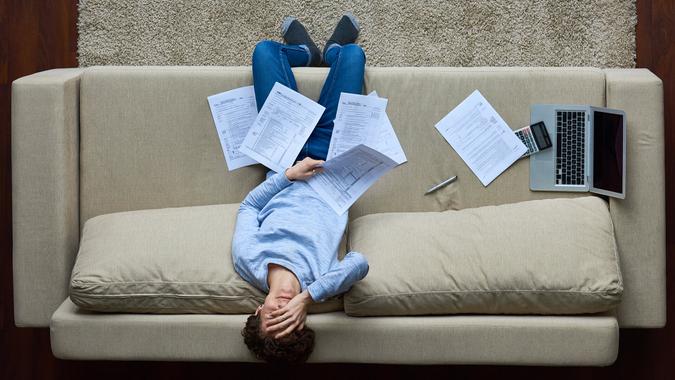 Failed woman leaning on sofa and covering face with hand, she holding business document.