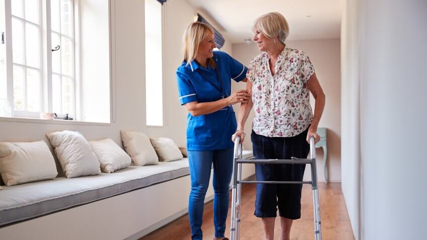 Nurse helping senior woman use a walking frame.
