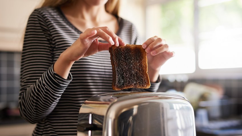 Shot of a woman removing a slice of burnt toast from a toaster at home.