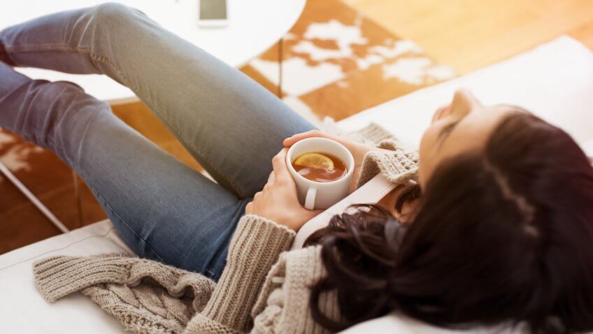 Young woman relaxing on sofa holding cup with lemon tea.