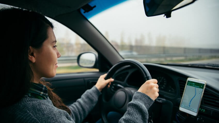 woman driving car by highway in foggy time using navigation on her phone.