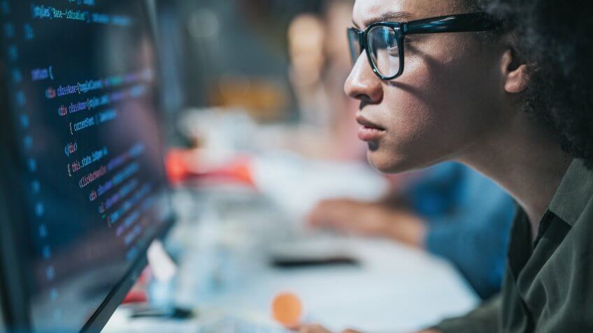 Focused black female programmer coding new computer language while working on desktop PC in the office.