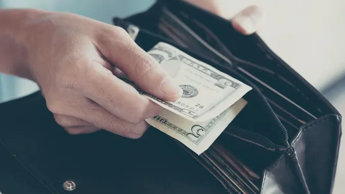 A woman pulling out five dollar bill from her wallet to show frugality or maximizing money.