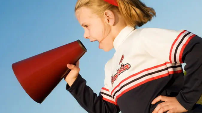young girl in cheerleader outfit yelling into a megaphone
