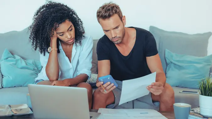 Young interracial couple in the couch stressed with financial problems doing calculations with paper work"n.