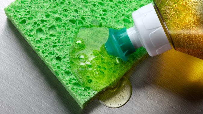 macro shot of dish soap being squeezed onto green sponge in aluminum sink.